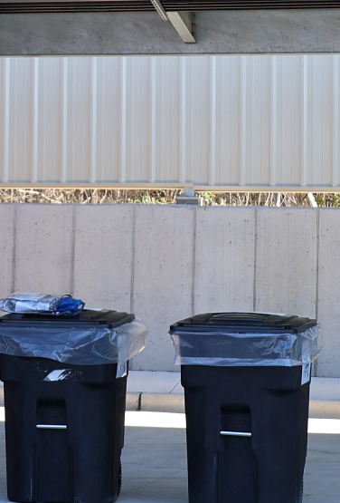 A blue recycling bin with a sign directing residents to recycle plastic bags.